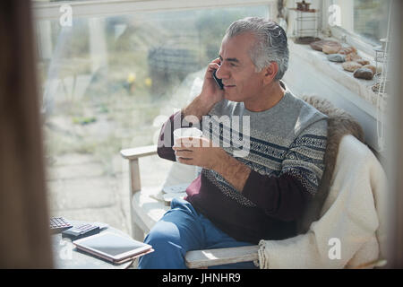 Senior man drinking coffee and talking on cell phone on sun porch Stock Photo