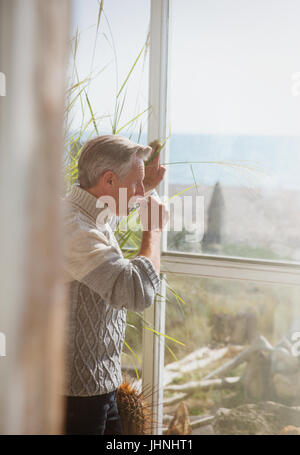 Senior man drinking coffee at sunny beach house window Stock Photo