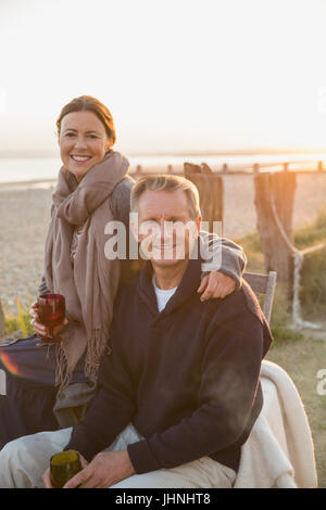 Portrait smiling mature couple drinking wine on sunset beach Stock Photo