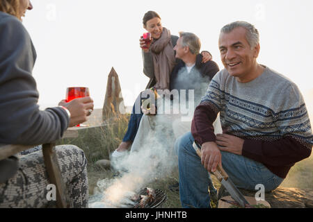 Mature couples drinking wine and barbecuing on beach Stock Photo
