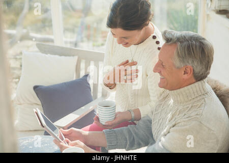 Mature couple drinking coffee and using digital tablet on porch Stock Photo