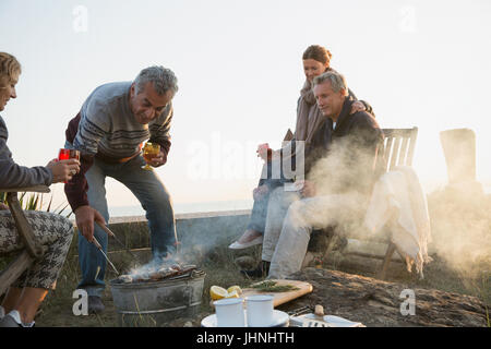 Mature couples barbecuing and drinking wine on sunset beach Stock Photo