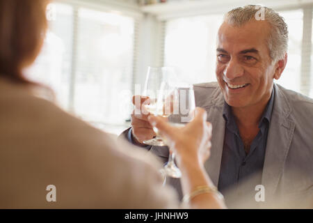 Smiling senior man drinking wine, toasting wine glasses with woman at restaurant Stock Photo