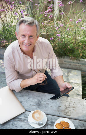 Portrait smiling senior man using digital tablet and drinking coffee at patio table Stock Photo
