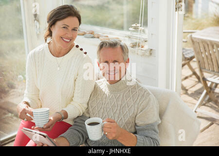 Portrait smiling mature couple using digital tablet and drinking coffee on sun porch Stock Photo