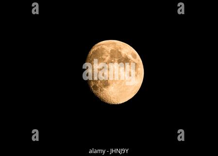 Horizontal photo of nice golden moon with visible craters on the edge of shadow. The moon is almost full with just small part hidden in the dark. The  Stock Photo
