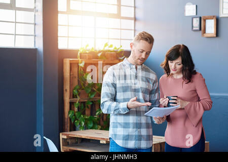 Two young work colleagues discussing paperwork together in an office Stock Photo