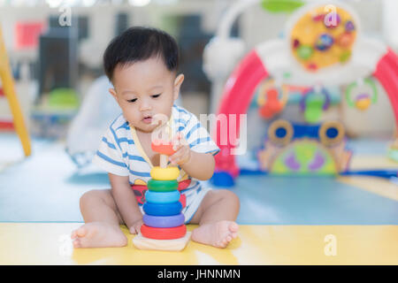 Adorable Asian baby boy 9 months sitting and playing with color developmental toys in kids room at home. Stock Photo
