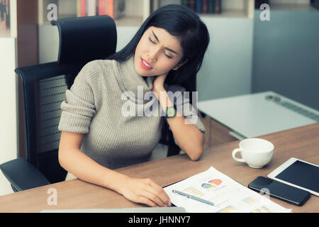 Asian young businesswoman having pain in her neck. Neck pain at office during working hard. Stock Photo