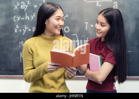 Asian woman student over blackboard holding and reading books togetherin classroom at university. Education concept. Stock Photo