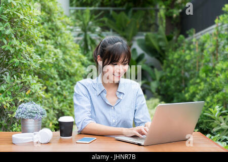 Asian woman in smiling face using laptop, workplace in tree garden. Concept of Asian woman lifestyle. Stock Photo