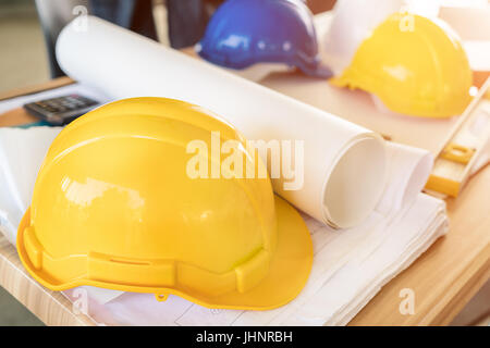 Engineer yellow helmet, calculator, level and project drawings on office table. Safety engineer concept. Stock Photo