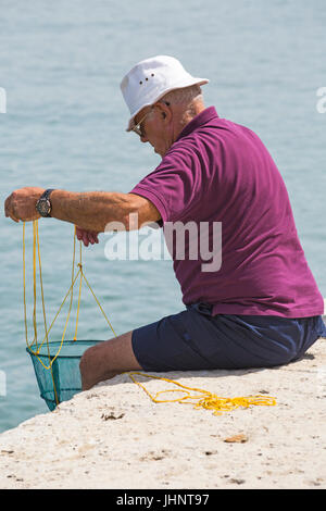 Man sitting on wall with basket net crabbing fishing at Lyme Regis, Dorset in July Stock Photo