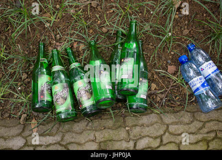 Empty Korean glass beer- and plastic water bottles lying on earth next to block-paved path. Pyongyang, DPRK / North Korea Stock Photo