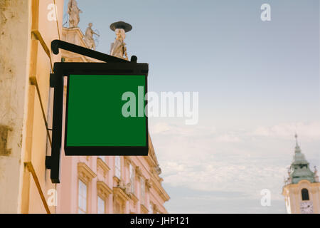 Blank square signboard, hanging from wrought iron bracket, in the city, classic architecture buildings background. Stock Photo
