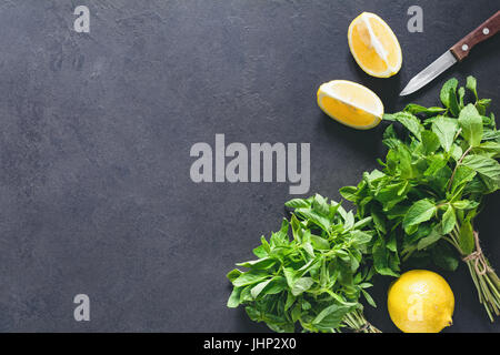 Fresh mint basil bunch and lemons on dark slate chalkboard background. Top view. Ingredients for summer refreshing drink cocktail Stock Photo