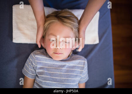 Overhead view of boy with eyes closed receiving neck massage from female therapist at hospital ward Stock Photo