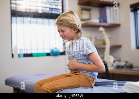 Boy sitting on bed with stomachache at hospital ward Stock Photo