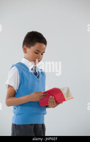 Attentive schoolboy reading book against white background Stock Photo