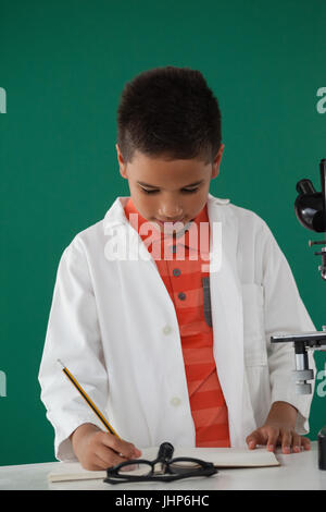 Schoolboy writing on book against green background Stock Photo