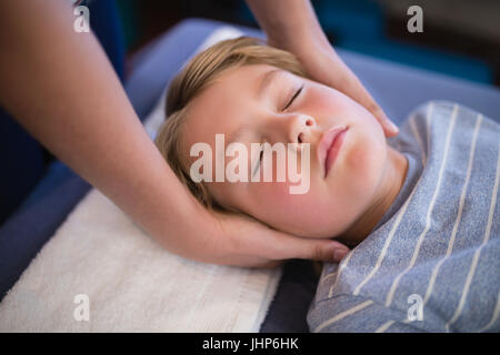 High angle view of boy with eyes closed receiving neck massage from female therapist at hospital ward Stock Photo