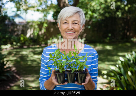 Portrait of smiling senior woman holding seedlings at backyard Stock Photo