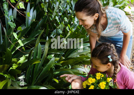 Woman looking while daughter sitting in wheelbarrow pointing towards plants at garden Stock Photo