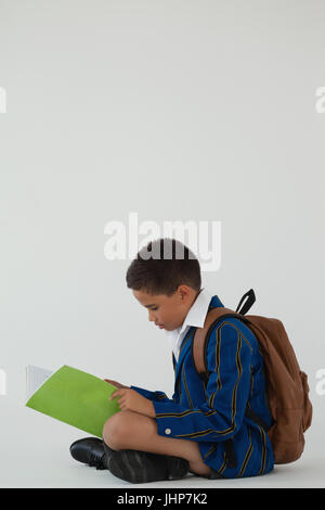 Attentive schoolboy reading book against white background Stock Photo