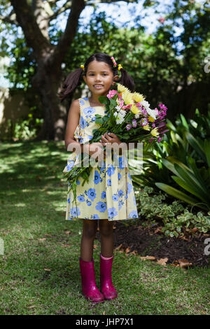 Portrait of smiling girl holding flowers bouquet standing in backyard Stock Photo