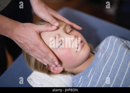 High angle view of boy lying with eyes closed receiving head massage from female therapist at hospital ward Stock Photo