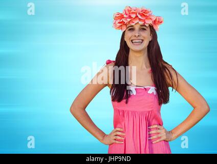 Digital composite of Millennial woman with flowers in hair and hands on hips against blurry blue background Stock Photo