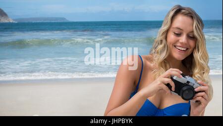 Digital composite of Millennial woman looking down at camera against beach Stock Photo