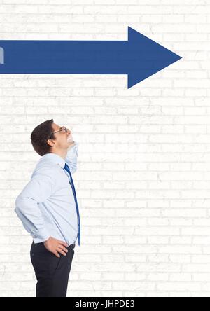 Digital composite of Business man looking up against white wall with blue arrow Stock Photo