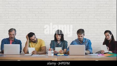 Digital composite of Business people at a desk looking at computers and tablets against white wall Stock Photo