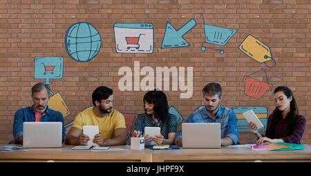 Digital composite of Business people at a desk looking at computers and tablets against brick wall with graphics Stock Photo