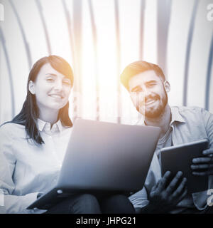 Business people sitting with laptop and tablet against white room with large window overlooking city Stock Photo