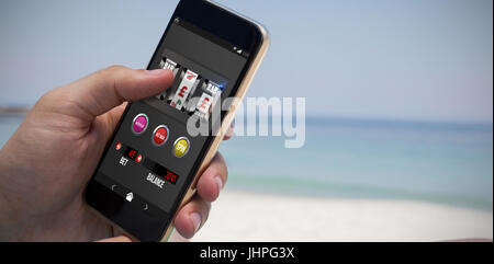 Casino slot machine on mobile display against close up of man using smartphone at beach Stock Photo