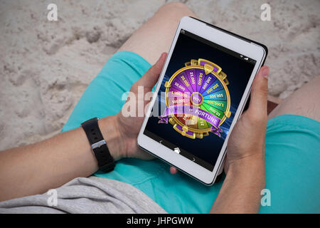 Colorful wheel of fortune on mobile display against man using digital tablet on the beach Stock Photo