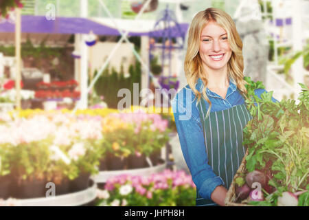Portrait of young woman holding vegetables in wicker basket against fake waterfall in garden center Stock Photo