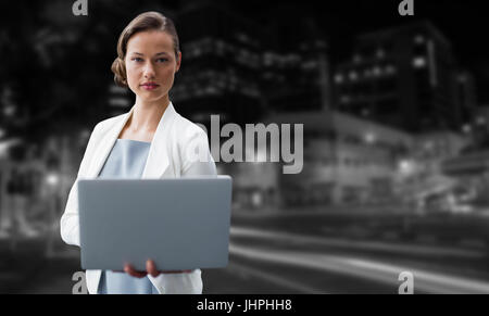 Portrait of businesswoman using laptop against illuminated roads by building in city Stock Photo