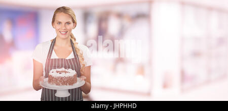 Portrait of young woman holding cake against modern reception desk Stock Photo