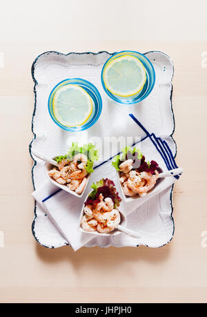 Prawn cocktail  in serving bowls in the form of hearts on a wooden table. On a white festive tray. Two glasses of water with ice Stock Photo