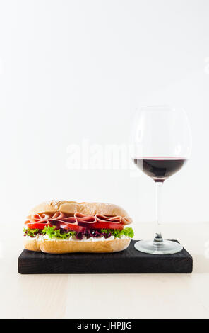 A Panini sandwich with ham, tomatoes and fresh lettuce leaves and a glass of red wine. white background, copy space Stock Photo