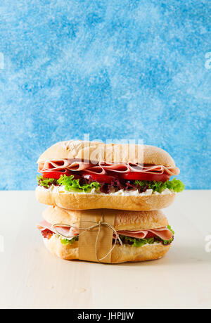 Italian healthy sandwich with tender ham, tomatoes, fresh lettuce leaves on a blue background.copy space Stock Photo