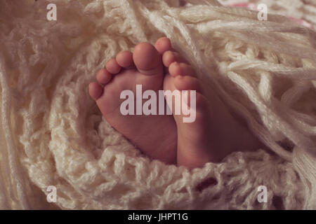 Small legs baby bundled up in a white knitted blanket Stock Photo