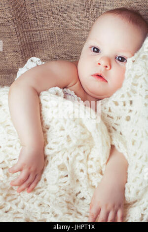 Child girl is wrapped in a white knitted blanket Stock Photo