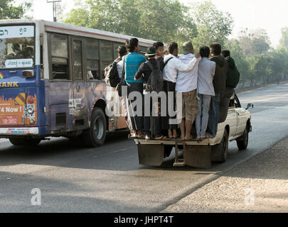 Overcrowded pickup truck moving alongside a bus on a highway in Yangon.  February 23, 2014 - Rangoon, Myanmar Stock Photo