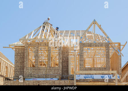 New house under construction, two workers installing roof truss. Stock Photo