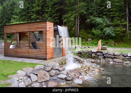 Artificial waterfall on a small wooden hut in a natural park in the dolomites in Italy Stock Photo