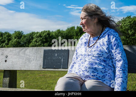 Elderly woman sitting on a bench, enjoying her retirement on a sunny day with a summer breeze blowing through her hair. Stock Photo